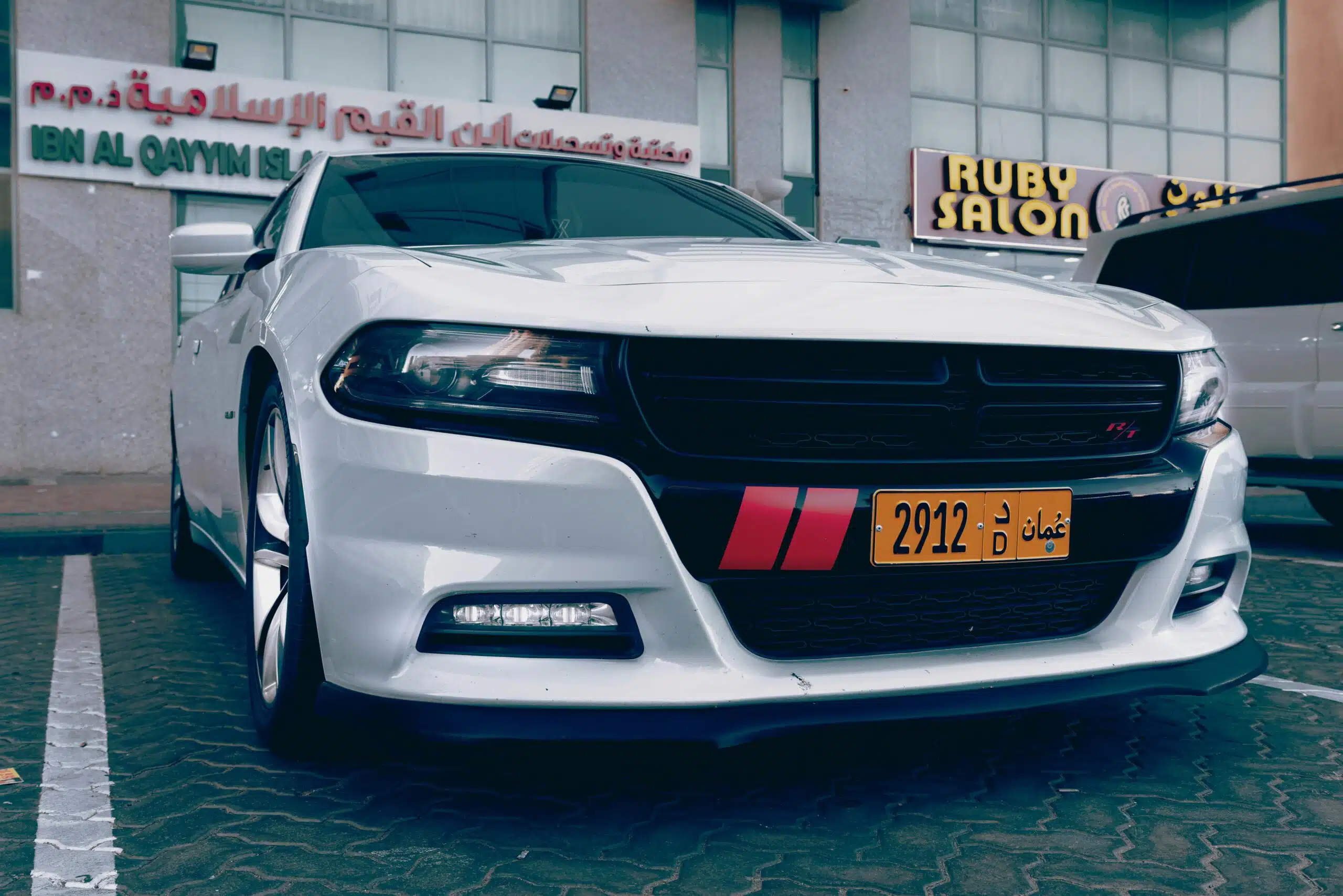Stylish white Dodge Charger parked outside a city building with Arabic signage.
