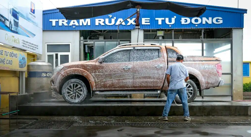A pickup truck being cleaned at a modern automated car wash facility with a worker present.
