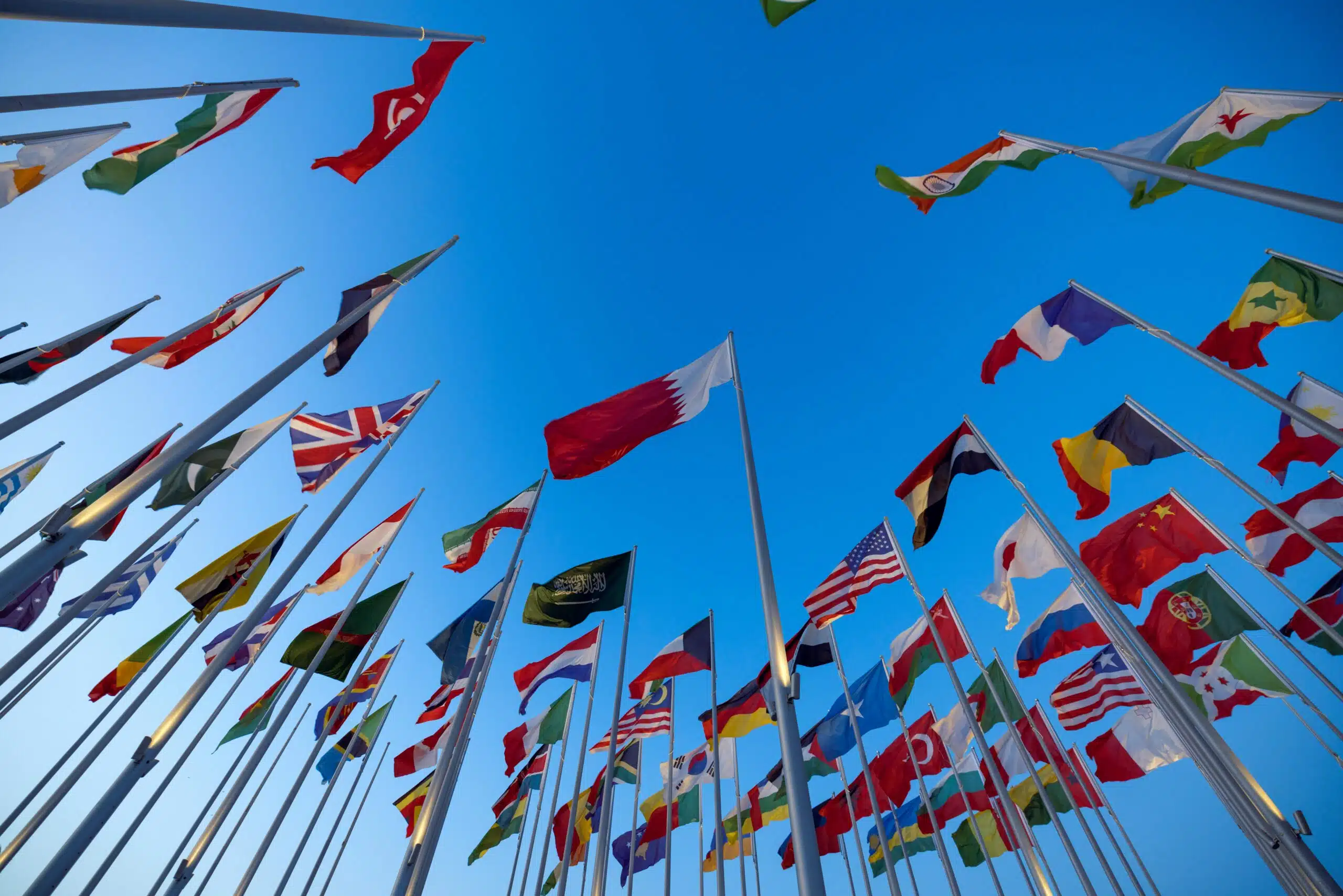 International flags waving against a clear blue sky in Doha, Qatar, symbolizing unity and diversity.