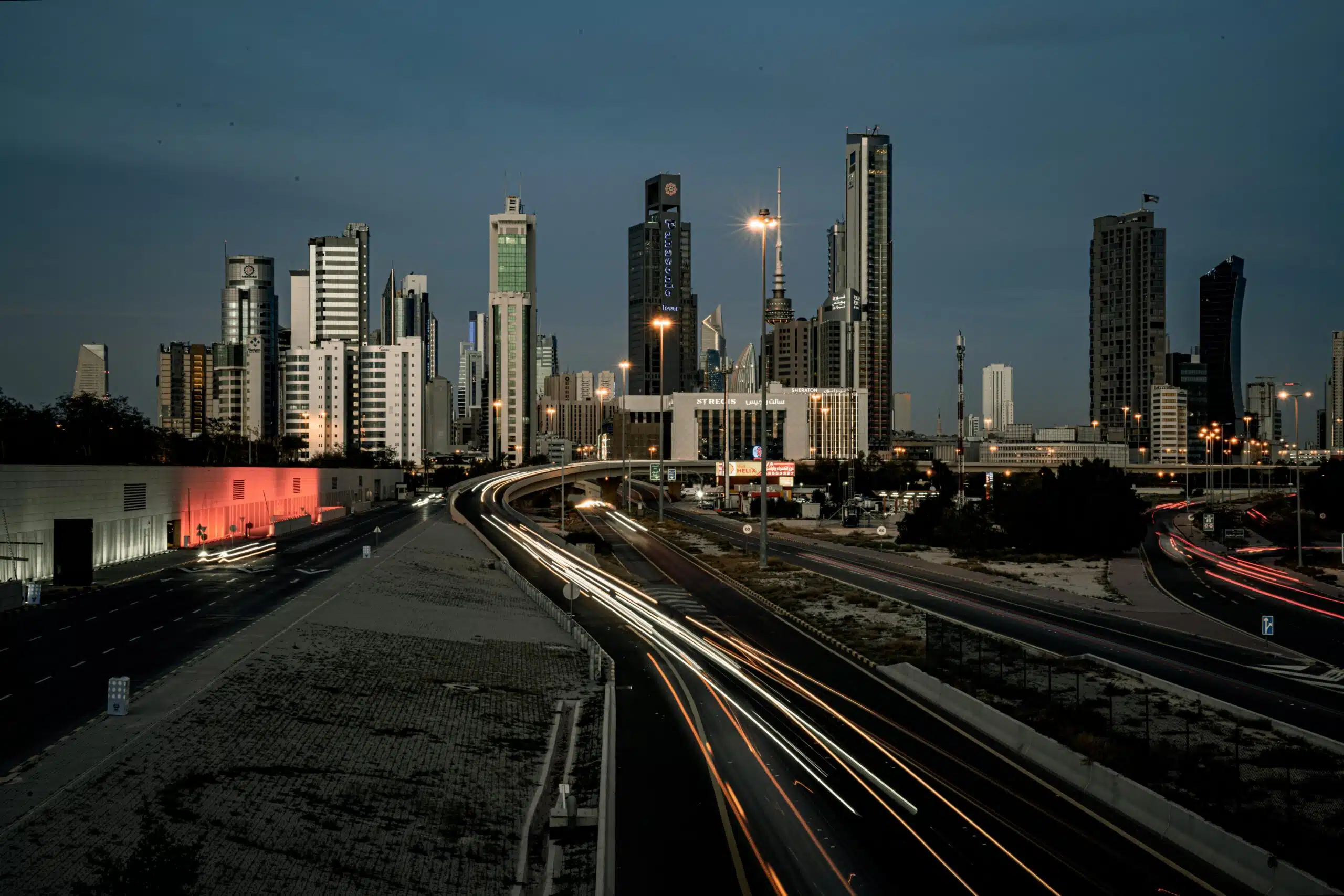 Twilight view of Kuwait City's modern skyline and streets with light trails.
