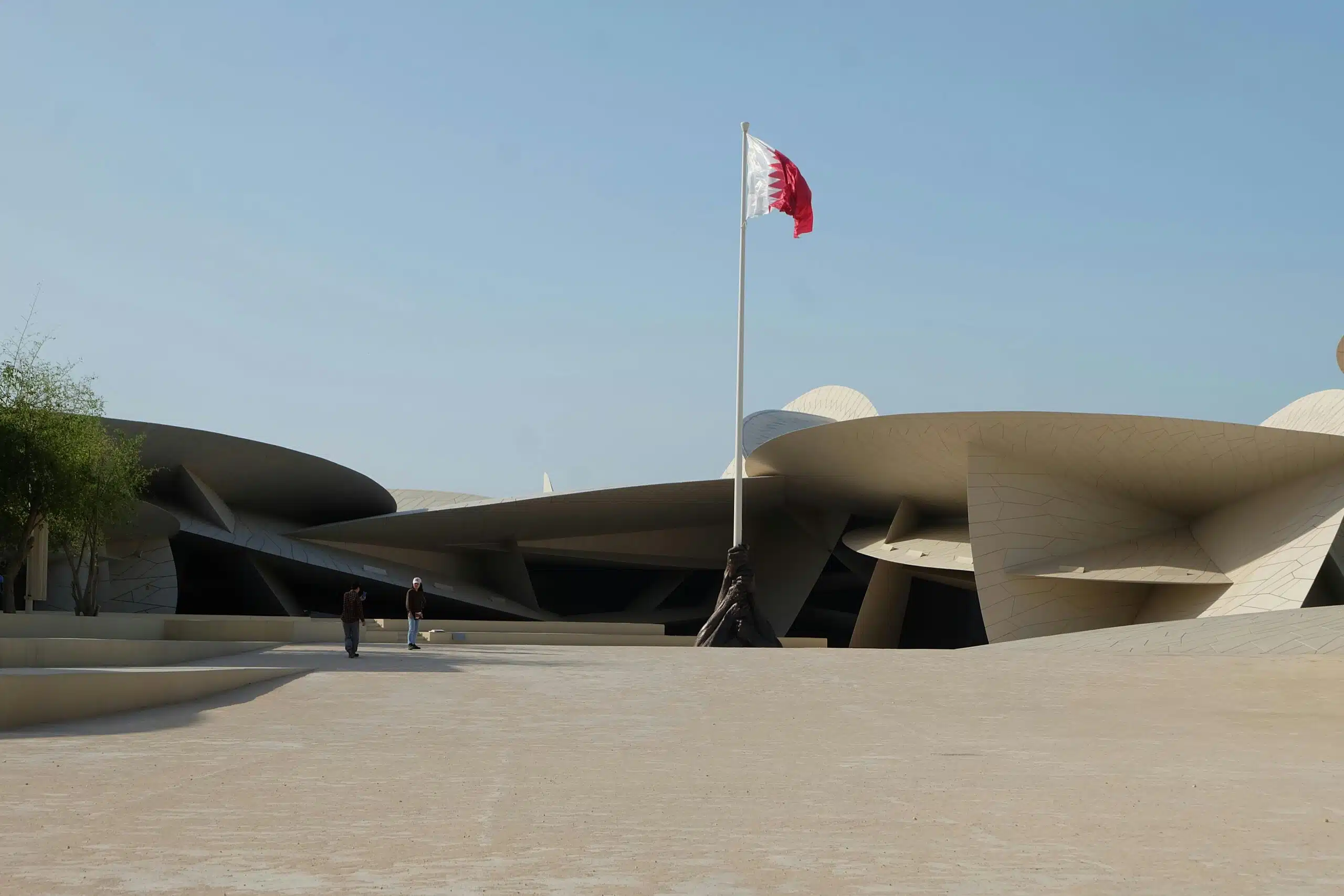 The distinctive design of the National Museum of Qatar with a Qatar flag against a clear sky.