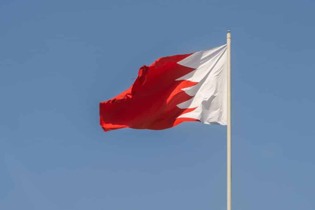The Bahrain national flag capturing the vibrant red and white design against a clear blue sky.