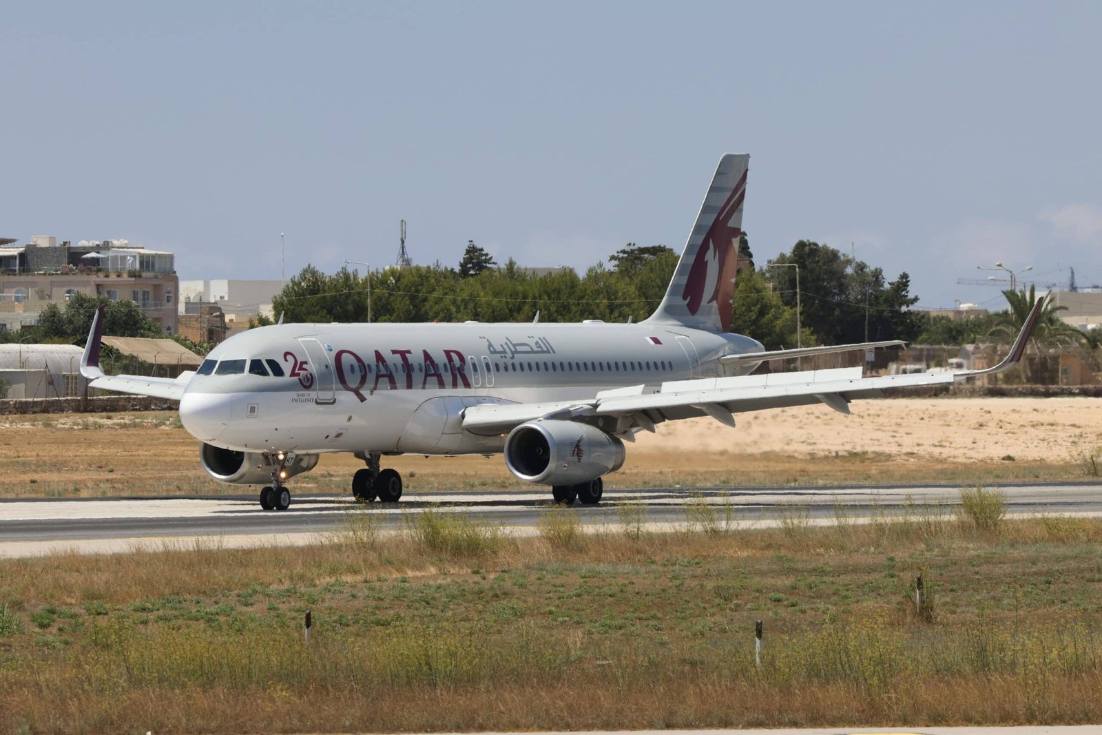 Qatar Airways Airbus A320 taxiing on runway with clear blue sky.