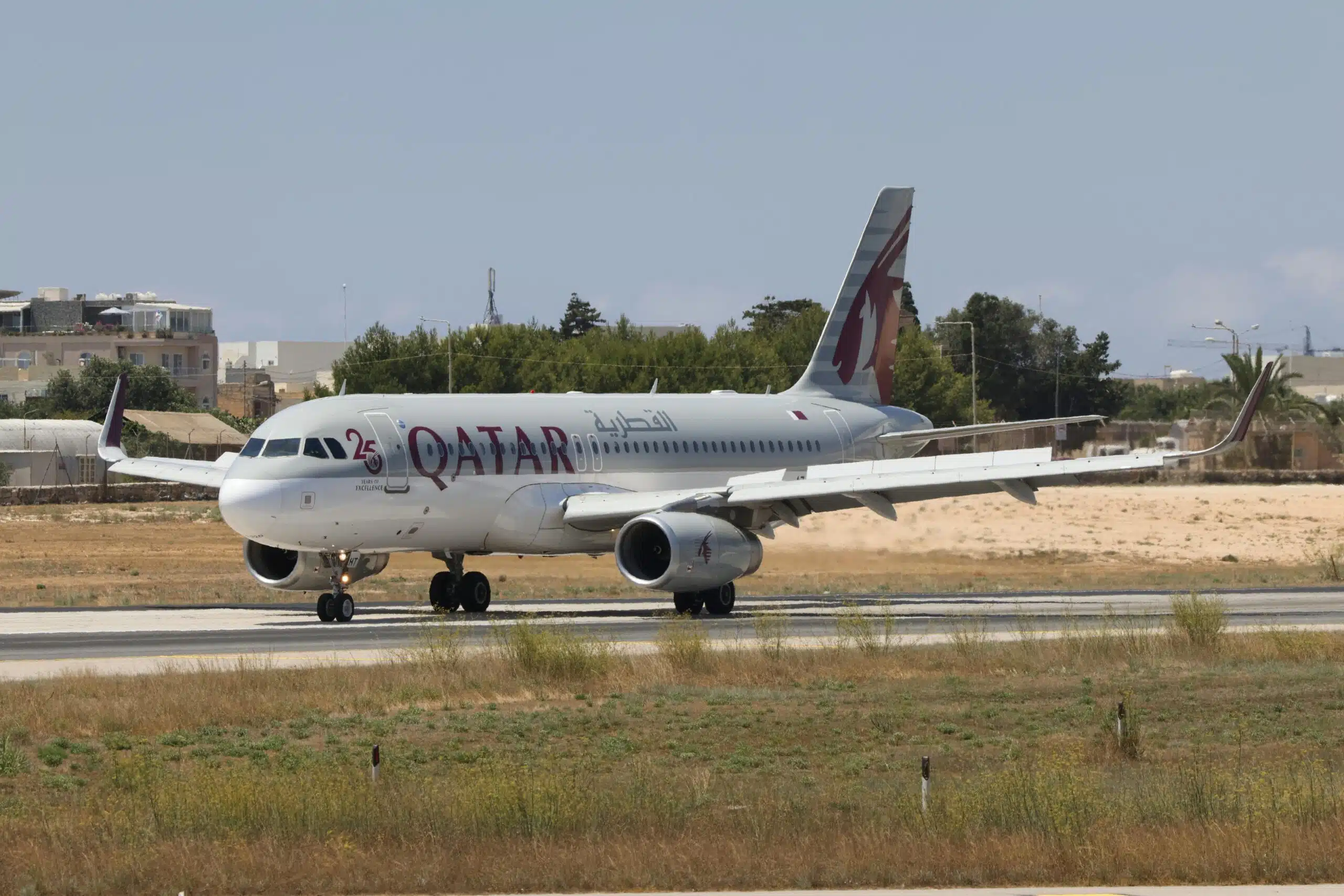 Qatar Airways Airbus A320 taxiing on runway with clear blue sky.