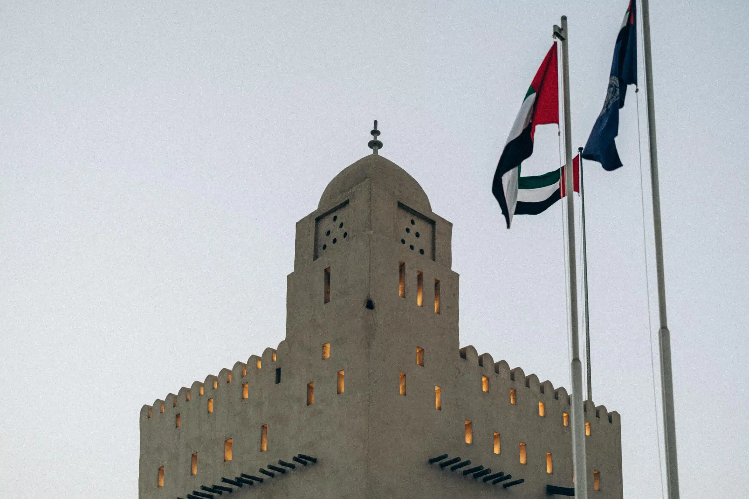 A traditional fortress with UAE flags at sunset in Abu Dhabi, showcasing architectural heritage.