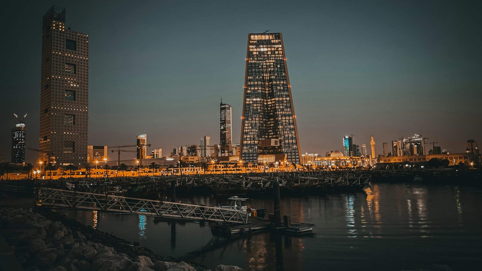 Stunning twilight cityscape featuring modern skyscrapers reflecting in water under a dusky sky.