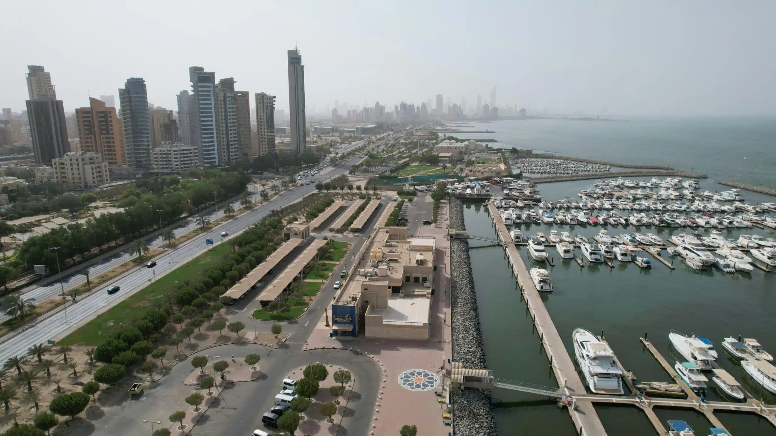 Aerial view of Kuwait City's modern skyline and bustling harbor with yachts.